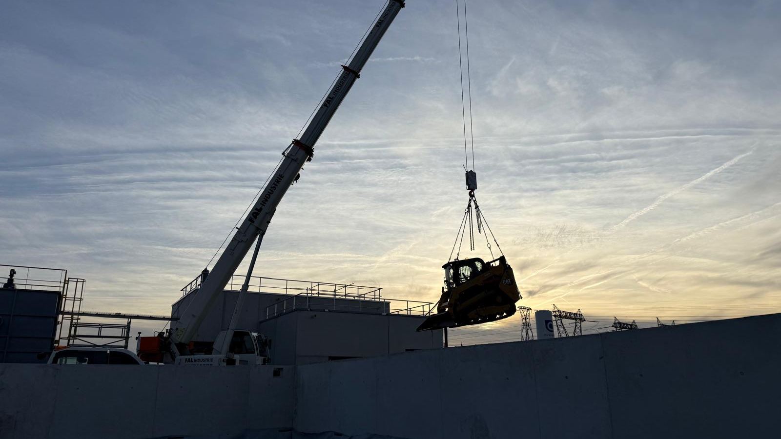 Grue de levage installant un engin sur un site industriel au couchant