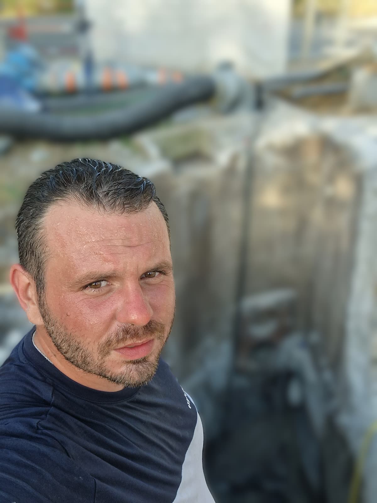 Un homme en tenue de chantier, au bord d'une fouille où sont posés des tuyaux et des regards béton