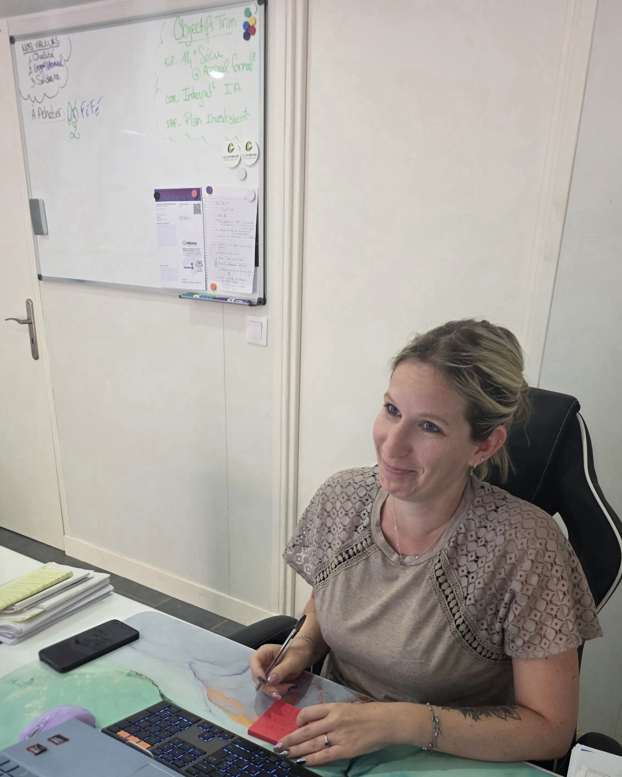 Sandy, associée de LEMAR, à son bureau, stylo en main, devant le tableau blanc des objectifs du trimestre